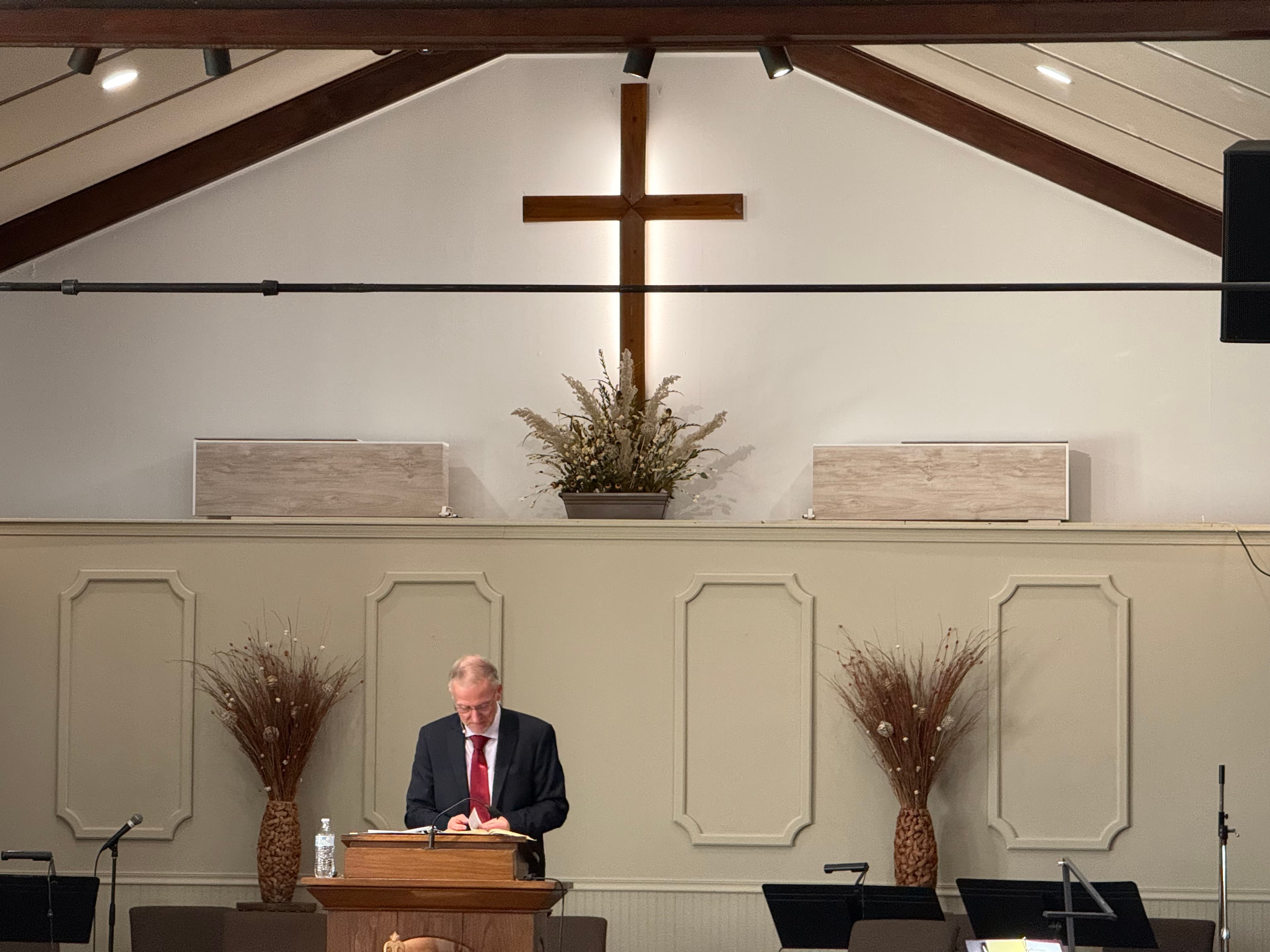 The minister preaching from the pulpit at Trinity Evangelical Church, beneath the wooden cross mounted on the sanctuary wall.