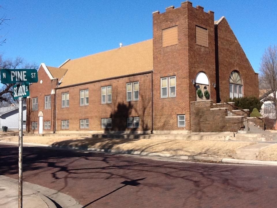 The red brick exterior of Trinity Evangelical Church, with its castellated tower and arched windows, seen from the corner of North Pine Street and School Street.